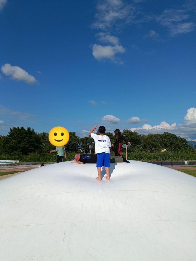 青空の下、ともぱ！たわらもとの大きなふわふわドームの上で跳んだり腹ばいになったりして遊ぶ子どもたち