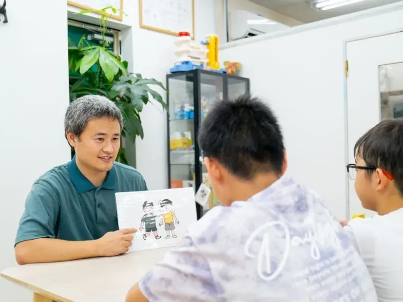 スタッフがイラストカードを見せながら、お子さまたちと場面について話し合う様子