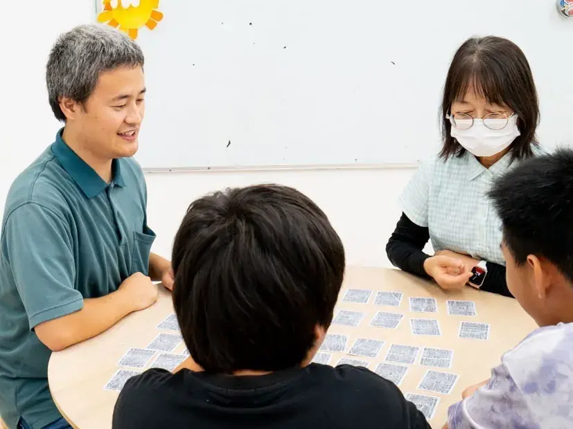 スタッフとお子さまたちがテーブルでカードゲームに取り組む様子